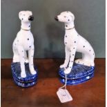 A pair of reproduction Staffordshire Dalmations, each in seated pose on blue oval base (21.5cm).