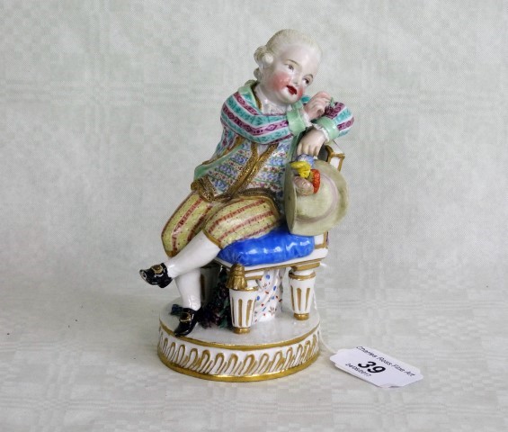 A Meissen figure of a seated finely dressed gentleman, a bunch of grapes beneath his chair,