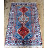 A small Eastern-style rug, having geometric patterns on a blue, red and mushroom ground,