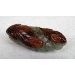 A celadon jade netsuke depicting a stylized amphibian beside a leaf, 6cm wide.