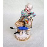 A Meissen figure of a seated finely dressed gentleman, a bunch of grapes beneath his chair,