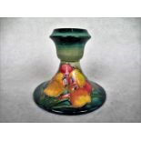 A William Moorcroft squat candlestick, having tube-lined floral decoration on a green ground,