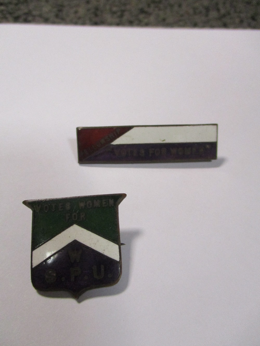 Two Suffragette enamel badges, 'Votes for Women W.S.P.U.' shield shape, and 'Fellowship Votes for