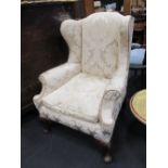 An upholstered wing back armchair on dwarf shell carved cabriole legs