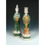 Two Tang pottery figures of attendants standing on hexagonal bases their hands clasped before them