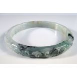 A jadeite arm bangle, the pale green stone with emerald inclusions, the rim carved in relief with