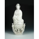 A blanc de Chine figure of Guanyin holding a rosary in her right hand as she sits on a triple