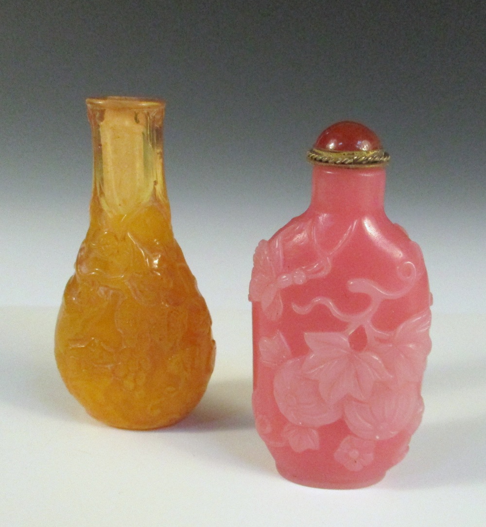 Two moulded glass snuff bottles and a stopper, the flattened bottle shape of the amber example