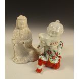 A blanc de Chine figure of Guanyin and a coloured porcelain figure of a boy, the deity seated