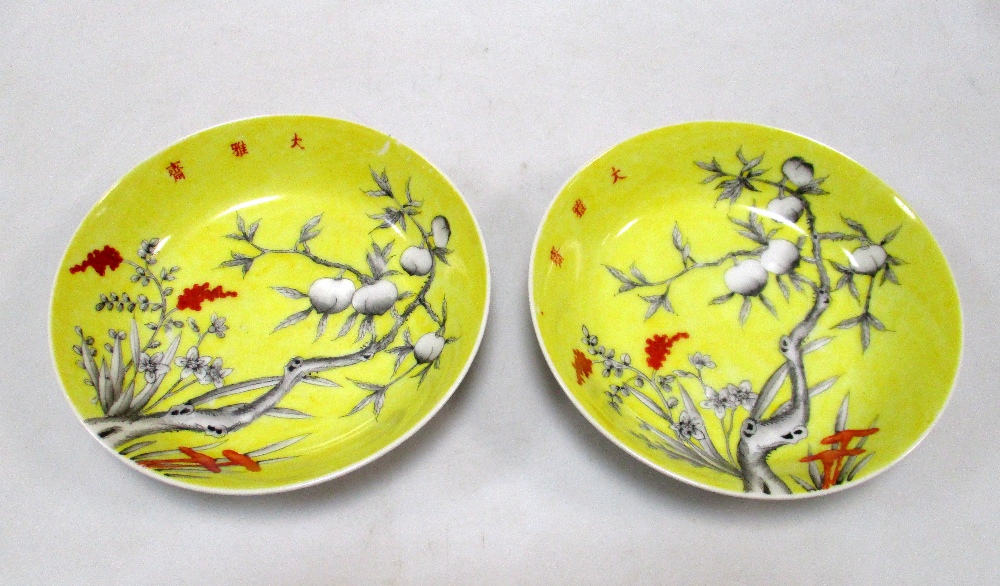 A pair of yellow ground saucers painted in grey with peaches, the heads of the millet and three