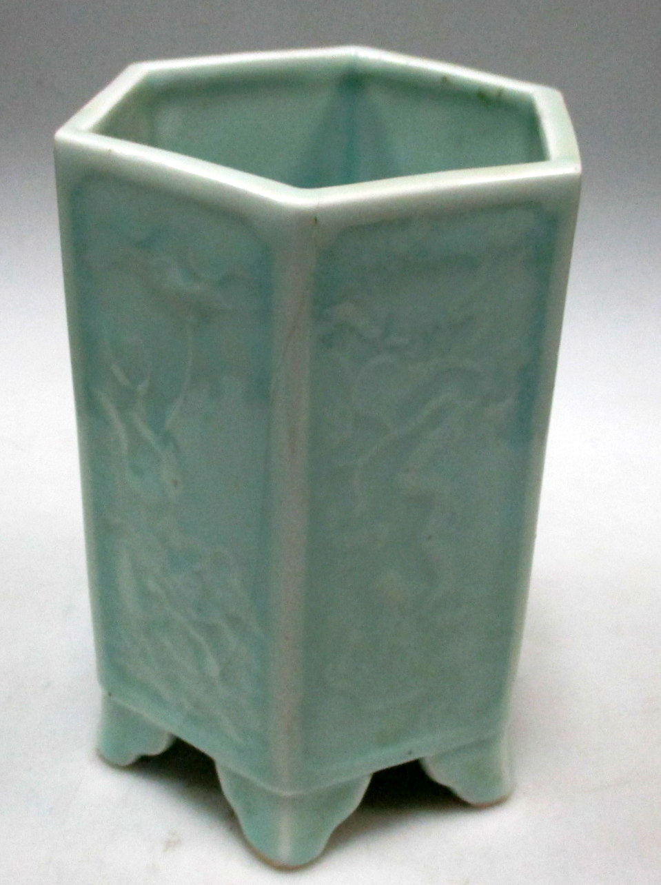 A pale celadon hexagonal brush pot, each side panel moulded in low relief with a different flowering