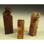 Three soapstone seals, the tallest of smokey brown stone surmounted by a Buddhist lion, one of the