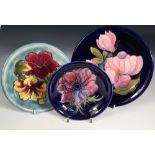 Thee modern Moorcroft plates, comprising a Magnolia pattern plate on blue ground, a Hibiscus pattern