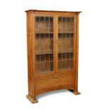 An Arts & Crafts glazed oak bookcase, the pair of leaded glazed doors above a fall-front cupboard,