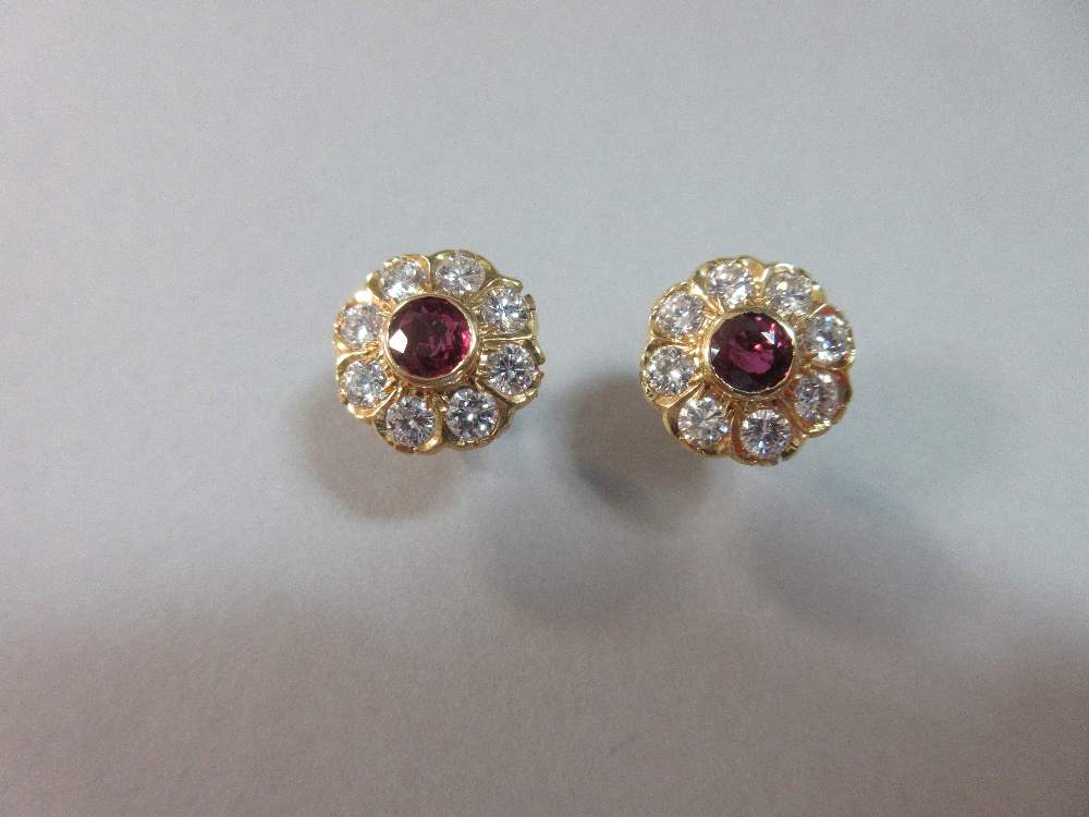 A pair of rhodolite and diamond flowerhead earstuds, each round cut rhodolite garnet collet set in a