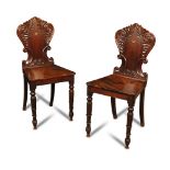 A pair of late Regency mahogany hall chairs, with leaf and scroll carved backs and panel seats, on