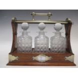 An oak cased three bottle tantalus with key and white metal handle and corner brackets