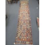 A North West Persian runner or carpet with geometric motifs on a rust red ground 490 x 197 cm