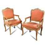 A pair of Regence limed walnut armchairs, with open arms, rocaille and scroll carved decoration (