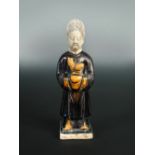 A Ming pottery figure of a lady, she stands wearing aubergine robes with an ochre cockerel held to