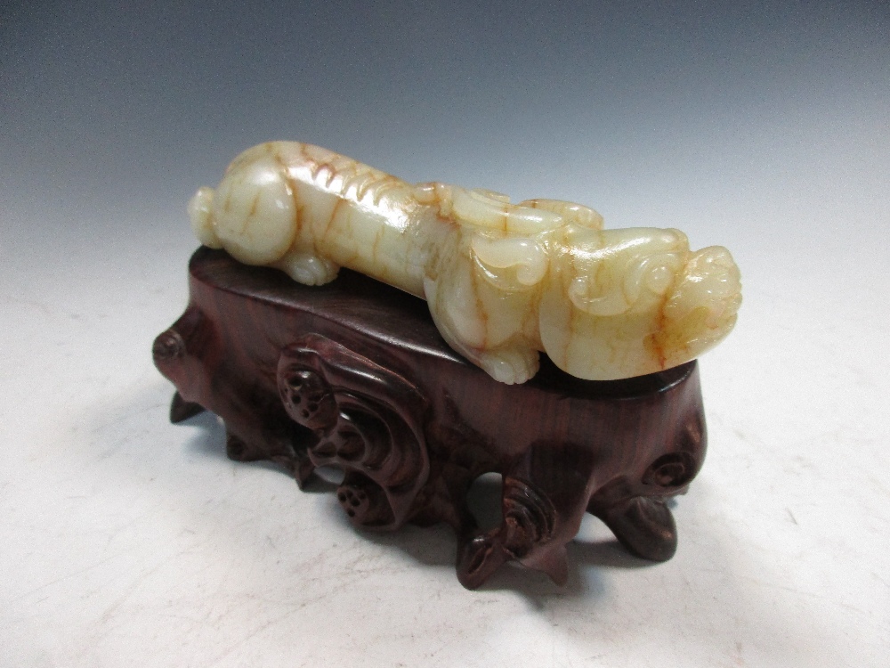 A jade qilin with wood stand, the pale green stone 'mud cracked' in brown and with black mossy