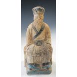 A Ming dynasty pottery seated figure, the dignitary with his hands clasped within his sleeves, his