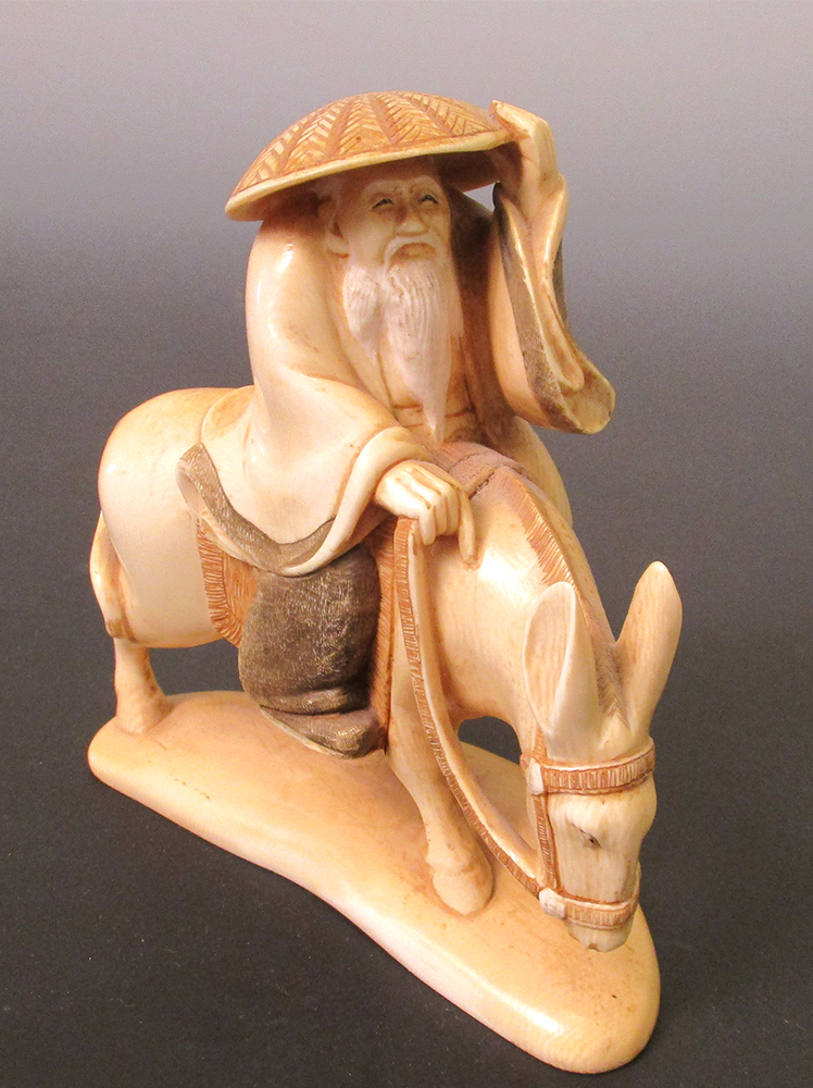 An early 20th century ivory figure of Fukurokuju riding a donkey with one hand on his straw hat