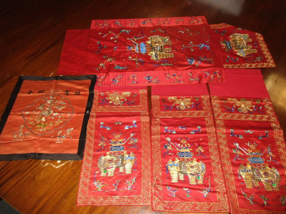 A set of four red silk panels and another, each of the set embroidered in gold thread with a