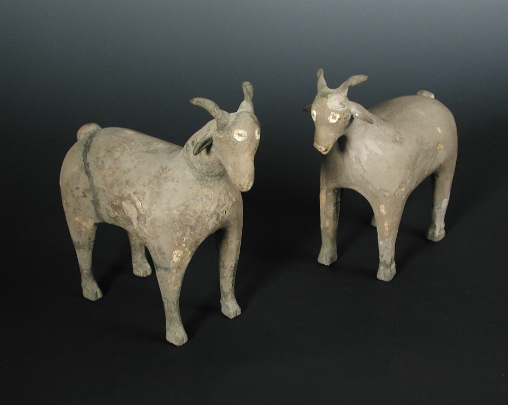 A pair of Han dynasty grey pottery goats, each characterful figure standing four square, its eyes
