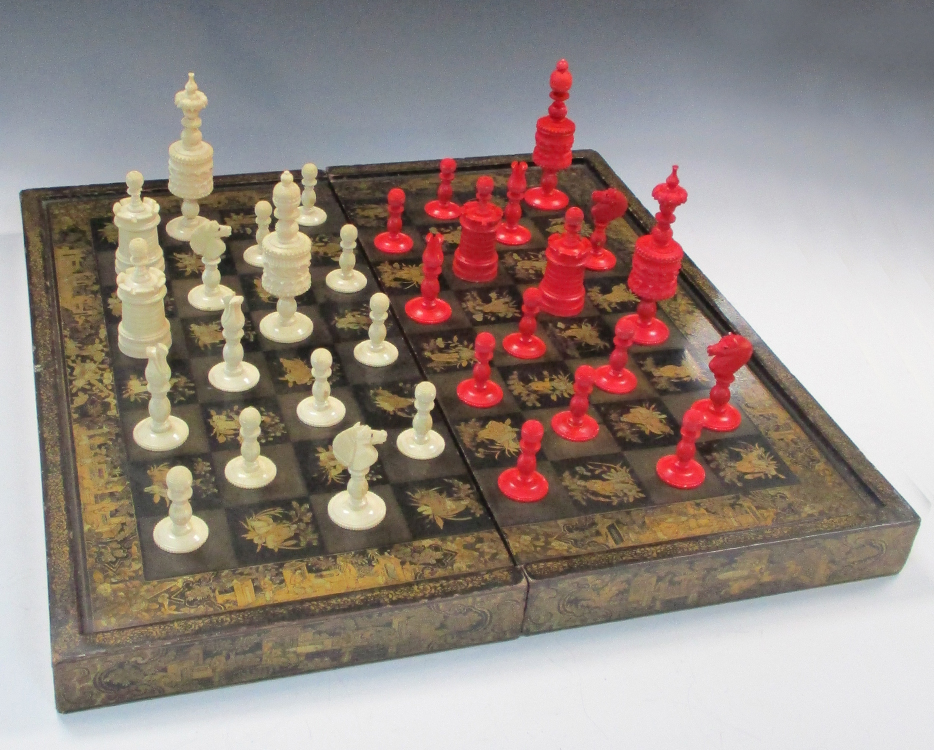A 19th century red and white bone chess set together with a lacquer board, the dark squares of the