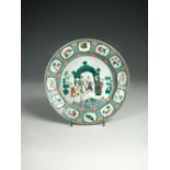 A famille rose plate, painted centrally with figures in a garden about a green arch, the green