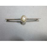 A natural pearl and diamond bar brooch, the plain narrow bar set to the centre with a half pearl