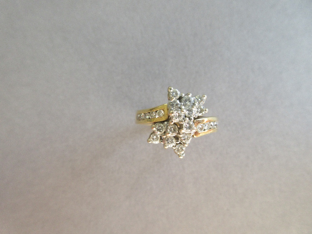 An asymmetrical diamond cluster ring, with a pierced bow form composed of tiered round brilliant cut