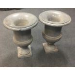 A pair of grey marble campana shaped urns, each with flared rim above turned body and raised on