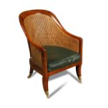 A Regency mahogany library bergere, caned back and seat with green leather squab cushion, on