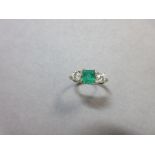 An emerald and diamond three stone ring claw set with a step cut emerald and two round brilliant cut