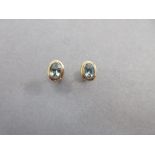 A pair of single stone aquamarine and gold earstuds, each oval cut aquamarine collet set to a tiered