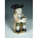 A 19th century toby jug, seated, holding a foaming jug of ale wearing a black tricorn hat, spotted
