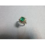 An emerald and diamond cluster ring, the emerald cut emerald four claw set in an oval of single