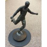 A spelter model of a footballer, cast mid-strike, mounted to a turned wood plinth and painted