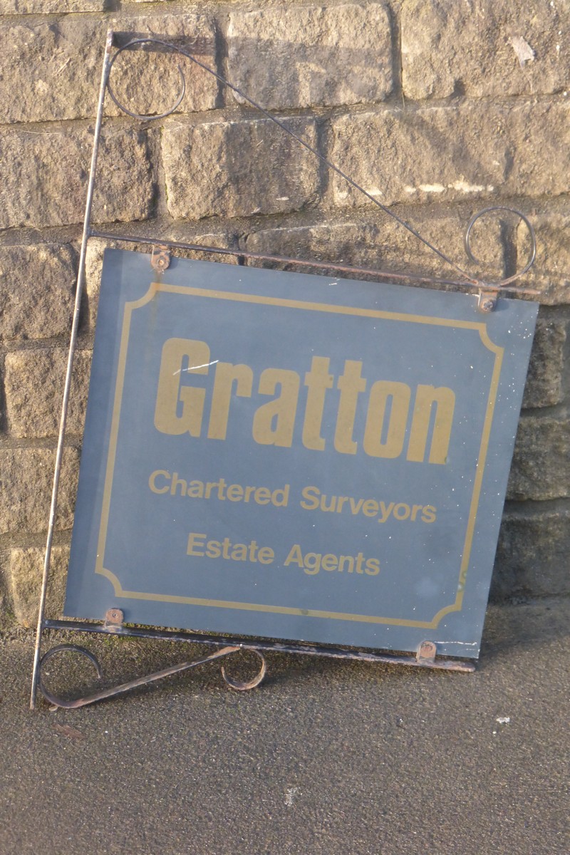 A double sided advertising sign on a metal wall bracket, promoting Gratton Chartered Surveyors and