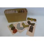 A box of military cloth trade badges, rank insignia and shoulder flashes attached to card (