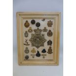 A framed display of 21 military cap badges including a Royal Lancaster Regiment 1st Volunteer