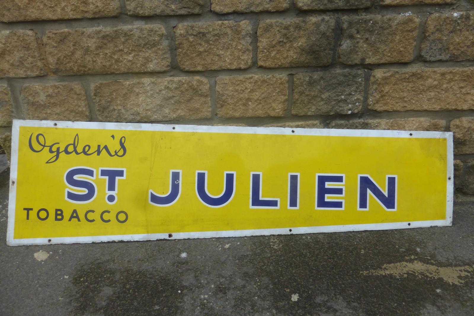 An Ogden's St. Julien Tobacco rectangular enamel sign, of tapering shape, 56 x 16"(max).