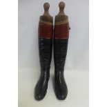 A pair of black leather gentleman's riding boots with wide tan leather bands, and wooden boot trees.