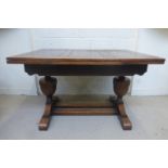 A 1930s oak drawer leaf dining table raised on large balluster shaped supports united by twin