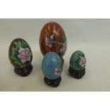 Four graduated cloisonne eggs on wooden stands.