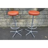 A pair of chromed circular bar stools with rust coloured upholstered seats.