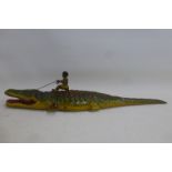 An unusual clockwork tinplate model of a crocodile with a figure sat on its back pulling up its