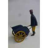 An early clockwork tinplate figure pushing a cart, possibly German.